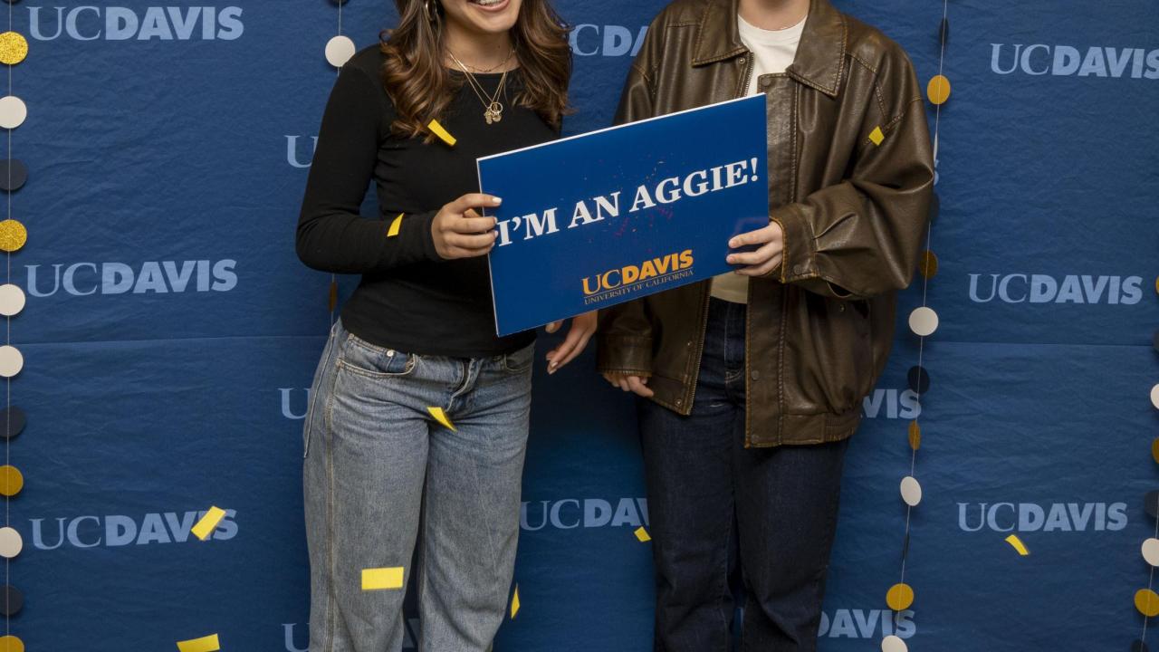 Two UC Davis admits posing for a photo in front of a celebratory backdrop.