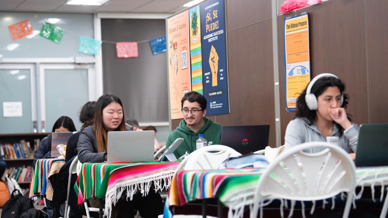 Five students sitting at tables in groups of two studying.