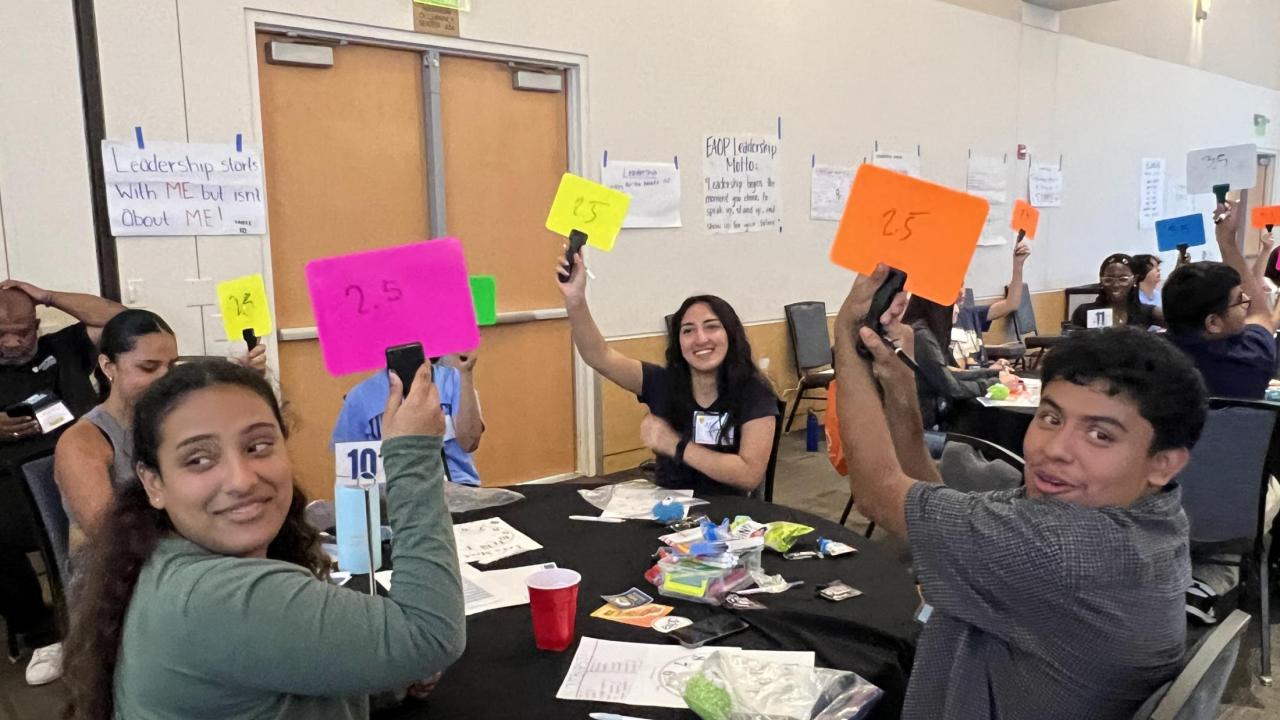 Students sit at round tables and hold up brightly colored number cards during an interactive activity at a leadership conference hosted by UC Davis EAOP.