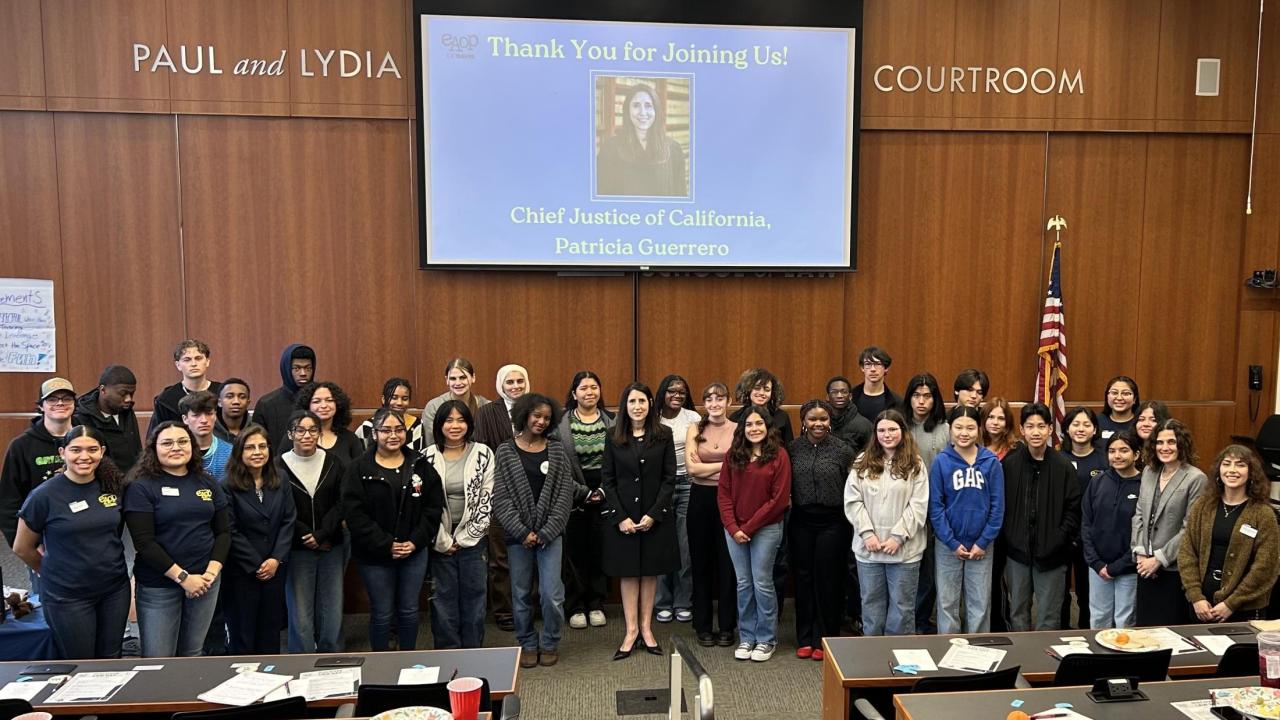 A group photo of students and staff standing in the UC Davis Paul and Lydia Courtroom during Discover Law Day. Chief Justice of California Patricia Guerrero stands in the center under a projected slide thanking her for joining the event.