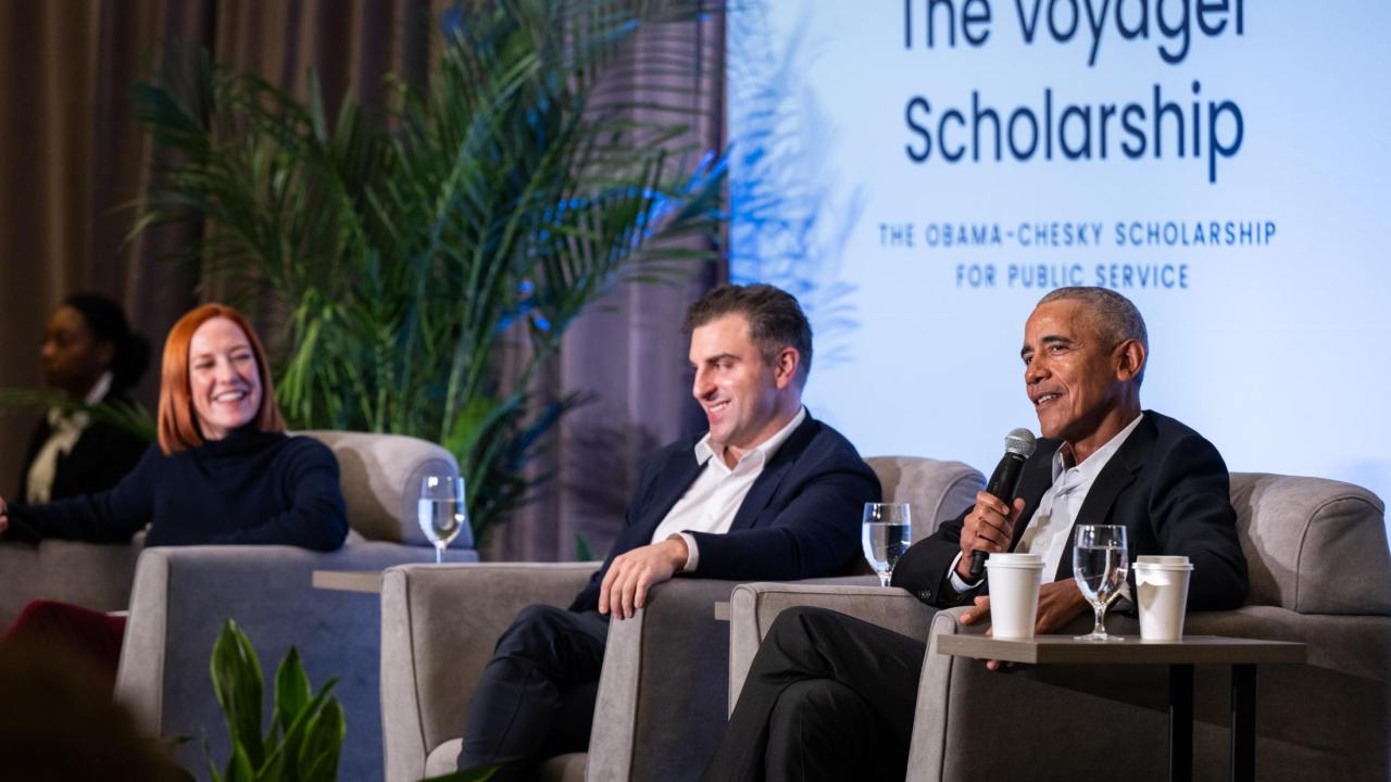 Former President Barack Obama alongside Airbnb Co-Founder and CEO, Brian Chesky and a panel moderator sit in chairs in front of a powerpoint titled The Voyager Scholarship.