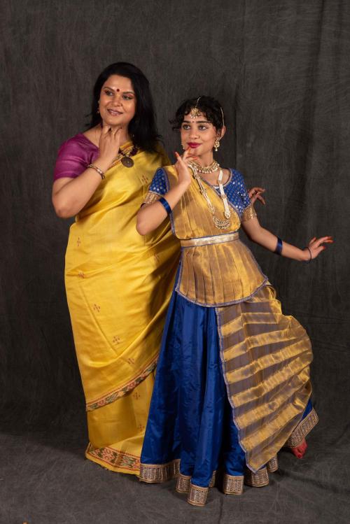 Vyoma and her dance teacher in traditional Kathak dance attire pose behind a plain grey backdrop.