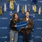 Two UC Davis admits posing for a photo in front of a celebratory backdrop. 