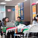 Five students sitting at tables in groups of two studying.
