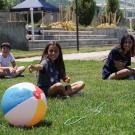 Three students sitting on grass looking over at a colorful beach ball.