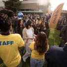 Admitted students and their families line up in small crowds at the Aggie Day check-in area, where staff in yellow t-shirts with blue writing that says staff help guide them into campus. 