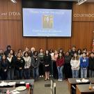 A group photo of students and staff standing in the UC Davis Paul and Lydia Courtroom during Discover Law Day. Chief Justice of California Patricia Guerrero stands in the center under a projected slide thanking her for joining the event.
